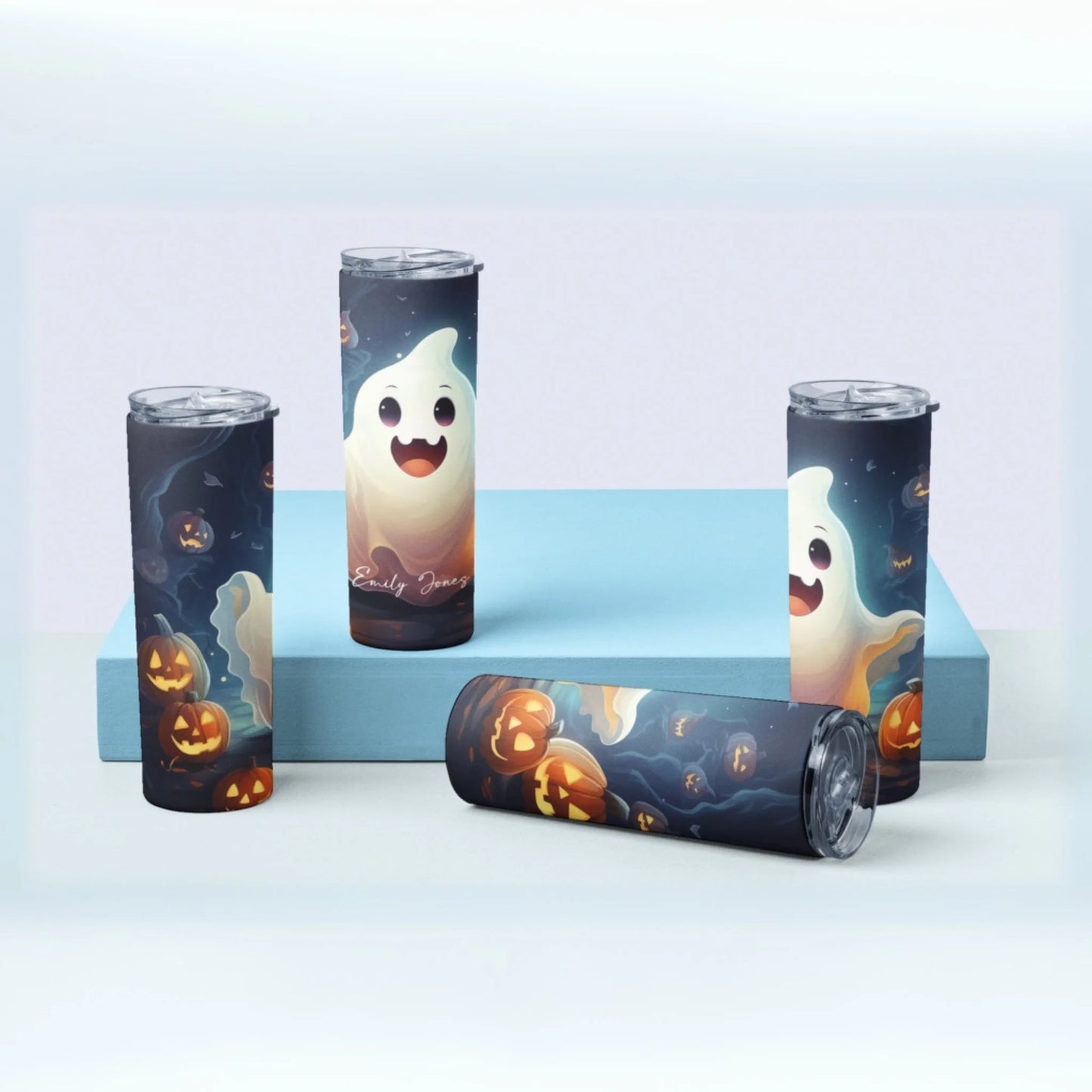 Four Ghost Personalized 20oz Skinny Tumblers – Halloween Cups with smiling ghosts and jack-o’-lanterns are displayed on a light blue platform, including one custom name tumbler lying on its side.